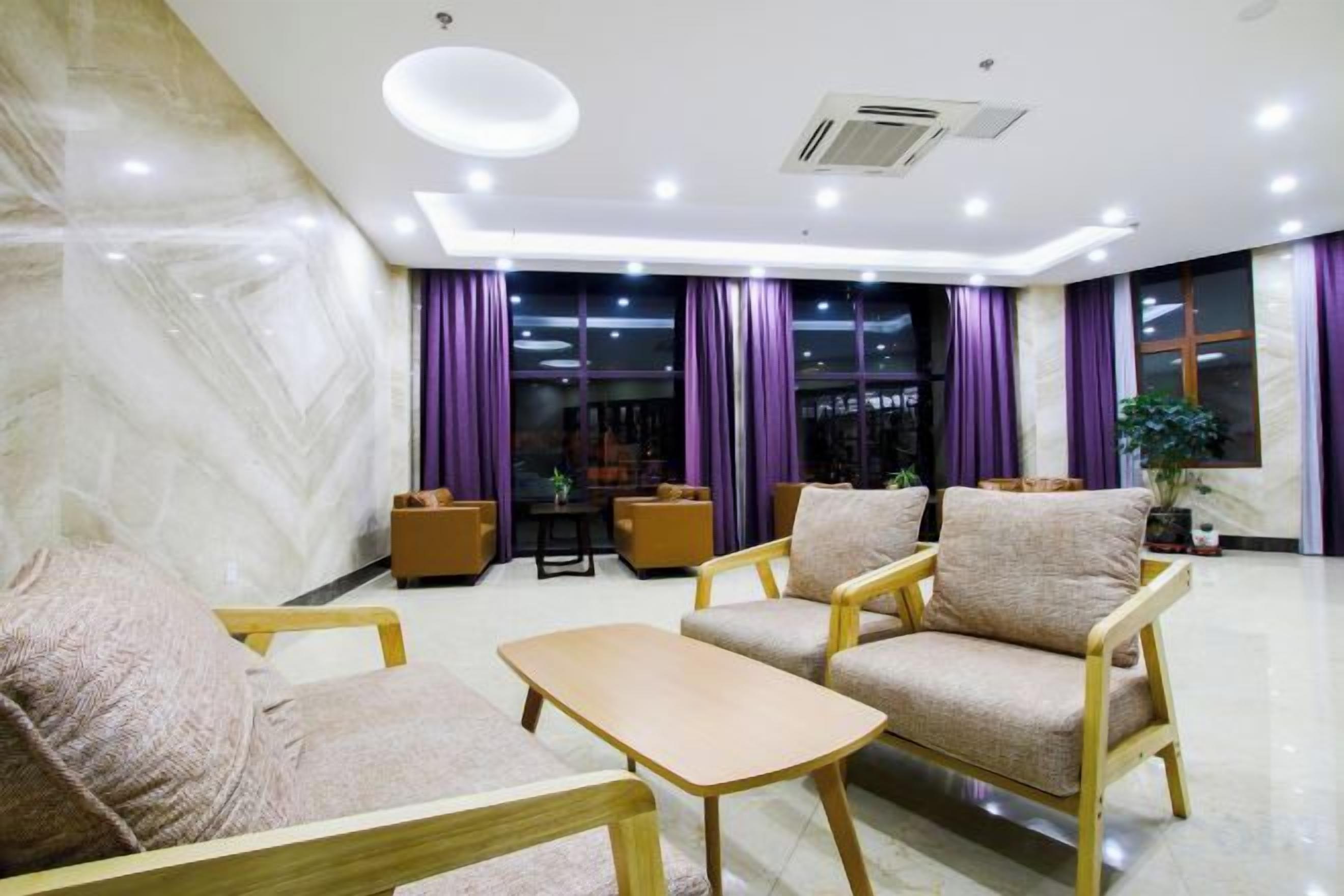 Un salón moderno con un conjunto de sofá, una mesa de centro y un televisor. Hay cortinas moradas y una planta al fondo.
