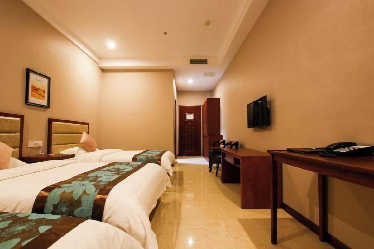 A hotel room with two beds, a desk, a chair, and a television.