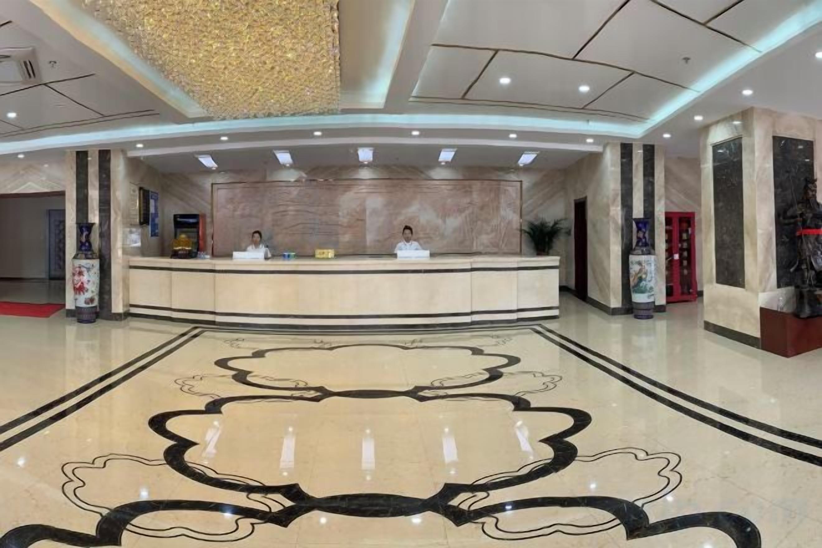 Zona de recepción de un hotel con suelo de mármol, mostrador de recepción y una gran araña.