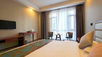 A hotel room with a large bed, a desk, a chair, a small table, and a TV mounted on the wall.