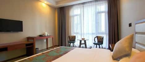 A hotel room with a large bed, a desk, a chair, a small table, and a TV mounted on the wall.