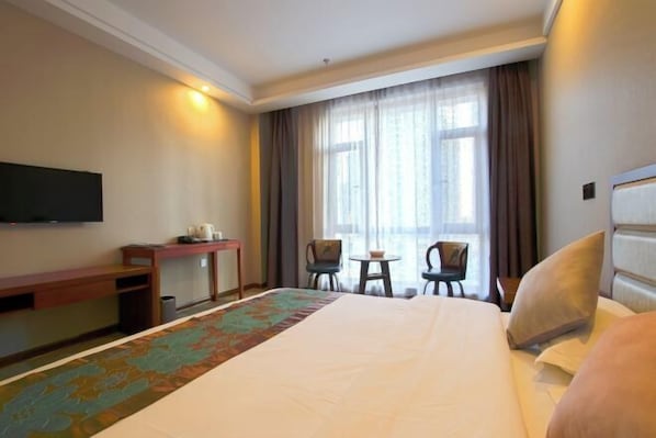 A hotel room with a large bed, a desk, a chair, a small table, and a TV mounted on the wall. - Jiaxi Hotel (Tongliao)