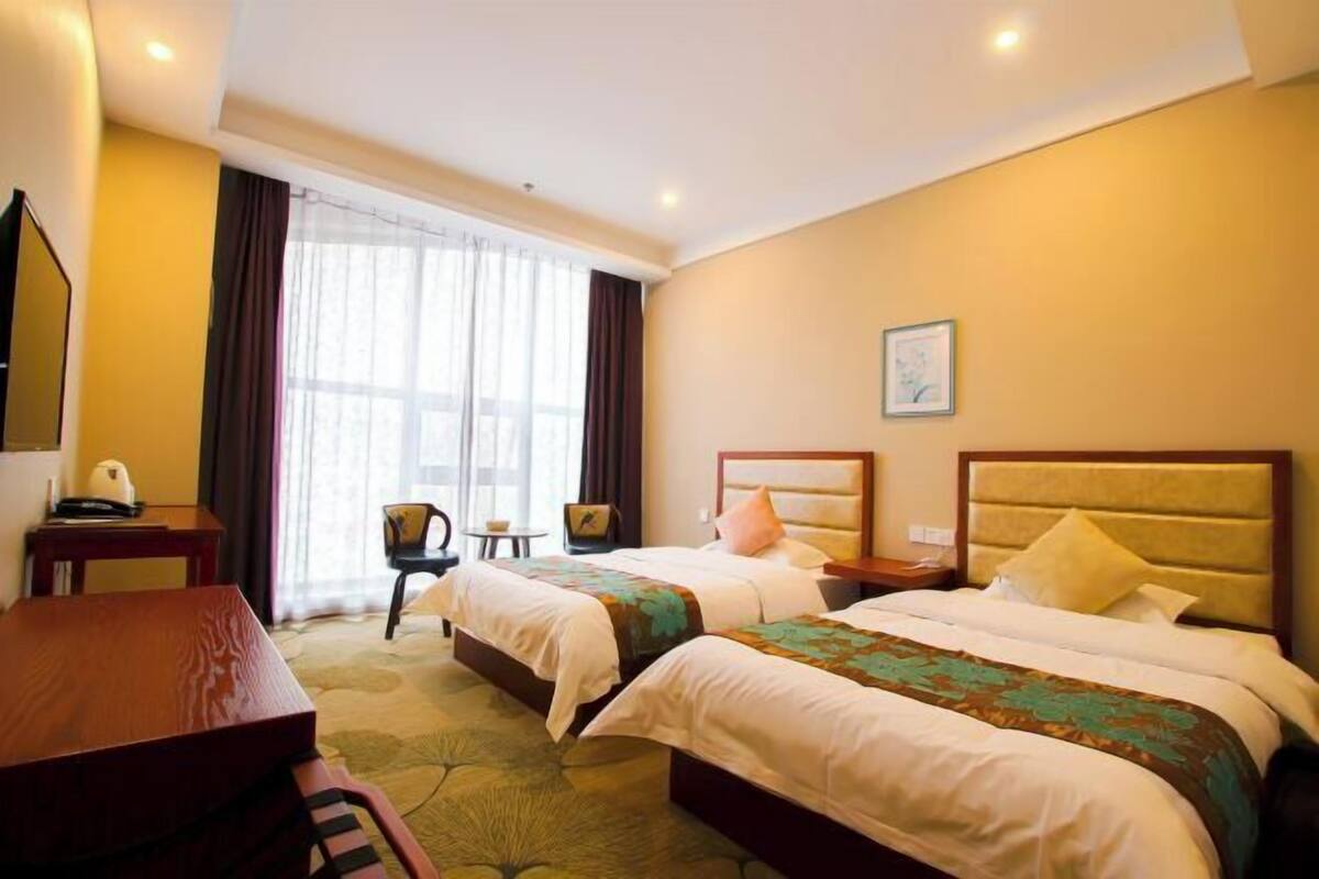 A hotel room with two beds, a desk, a chair, a small table, and a window with curtains.