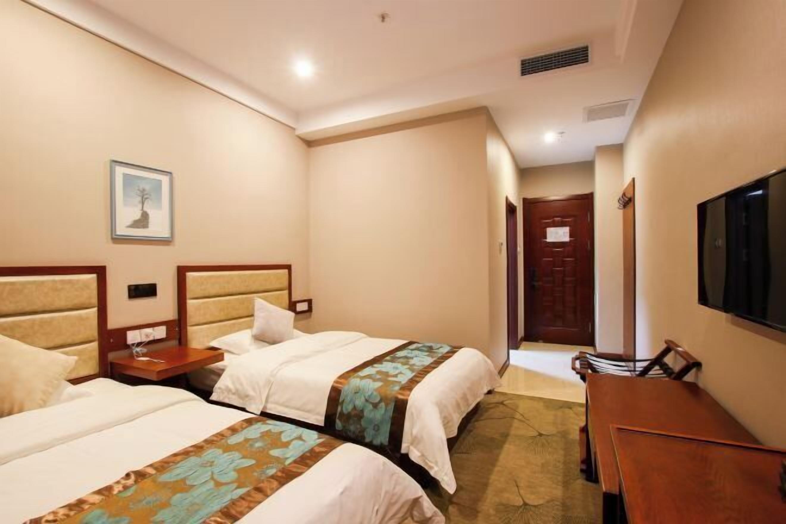 Una habitación de hotel con dos camas, un escritorio, una silla, un televisor y una puerta.