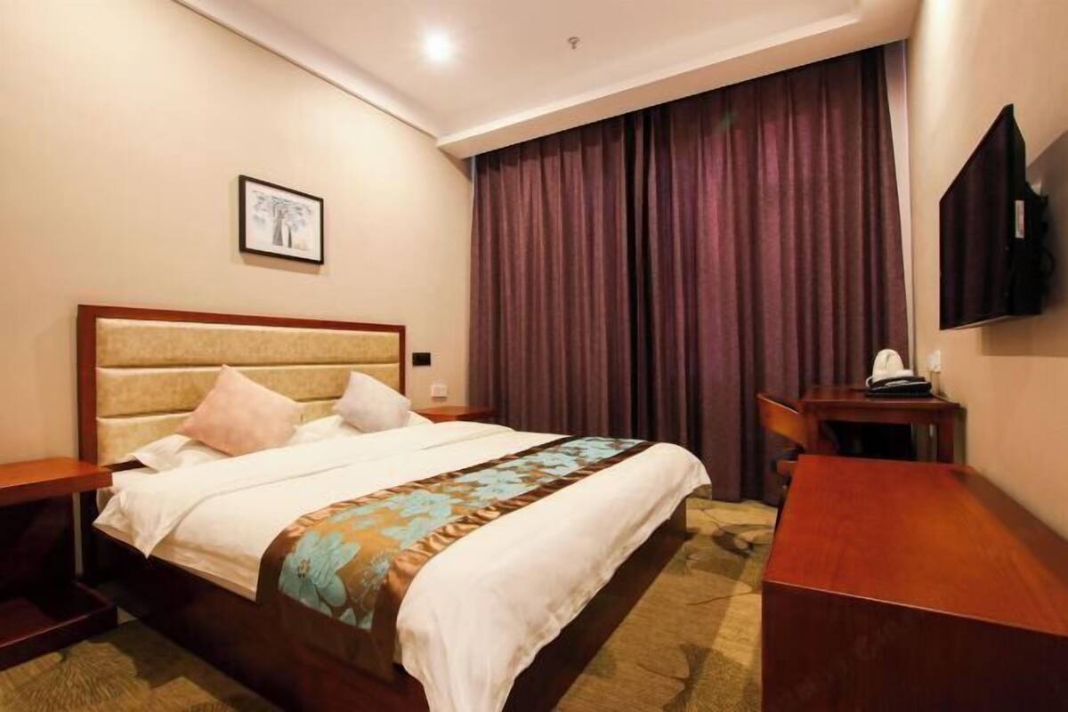 A hotel room with a bed, a desk, a chair, a television, and a picture on the wall.