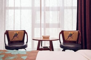 A hotel room with two chairs with bird designs, a small round table with a bowl, and a bed with a floral bedspread. - Jiaxi Hotel (Tongliao)