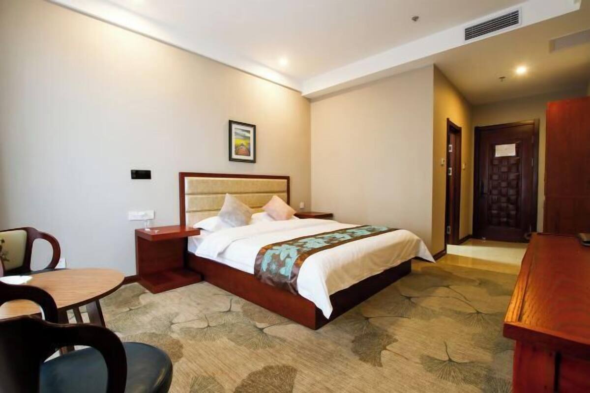 A hotel room with a bed, bedside table, chair, and a desk.