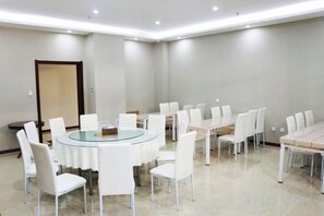 Uma sala de conferências com uma mesa redonda cercada por cadeiras, uma mesa retangular com cadeiras e uma porta ao fundo.