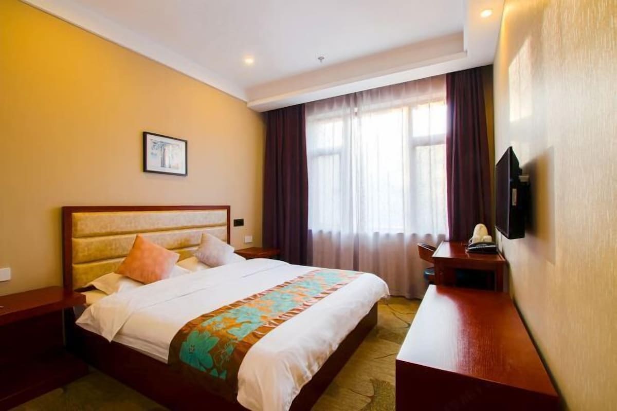 A hotel room with a bed, a bedside table, a TV, and a window with curtains.
