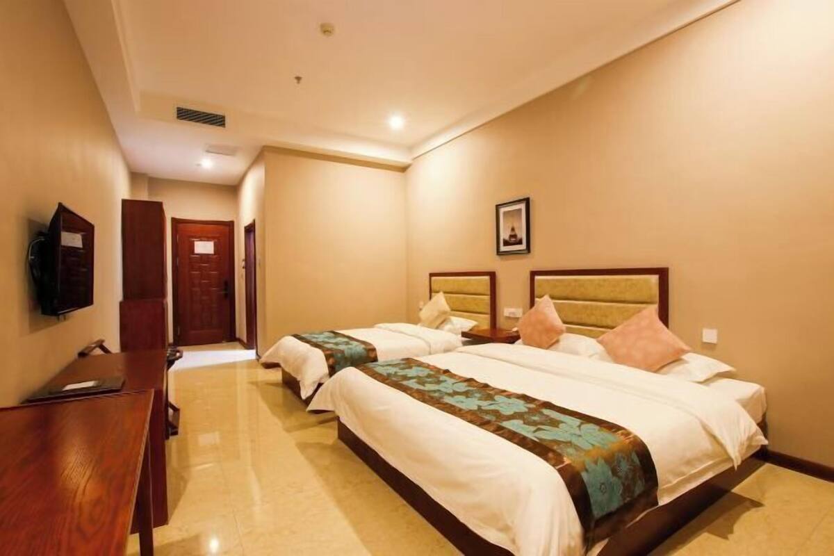 A hotel room with two beds, a wooden desk, a flat-screen TV, and a framed picture on the wall.