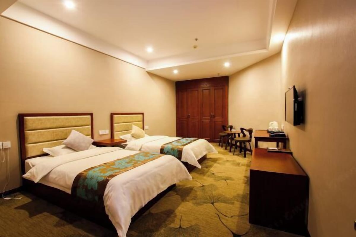 A hotel room with two beds, a desk, a chair, a TV, and a wardrobe.