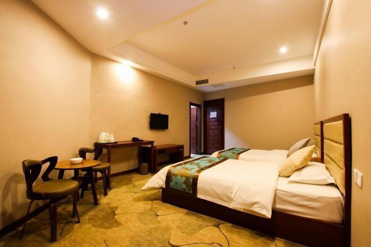 A hotel room with two beds, a desk with a chair, a television, and a carpeted floor.