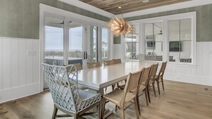 A spacious dining area with a large white table, wicker chairs, and a unique ceiling light fixture.