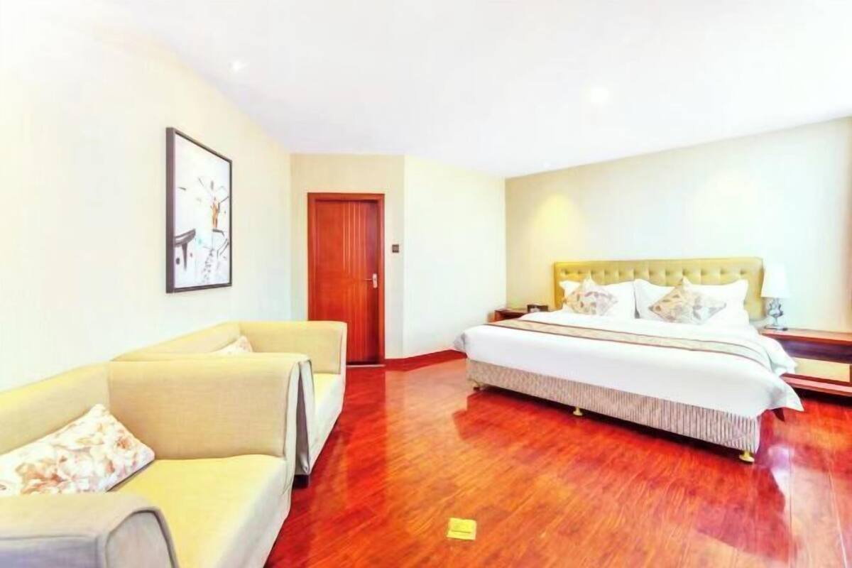 A hotel room with a bed, a sofa, a wooden floor, and a door.
