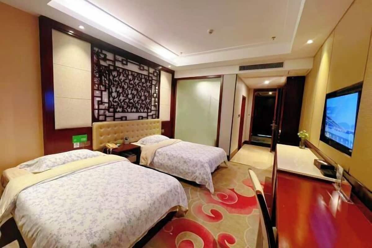 A hotel room with two beds, a television, a decorative wall panel, and a carpeted floor.