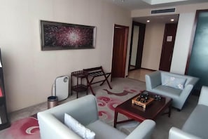 Habitación de hotel con sofá, sillones, una mesita de centro, un cuadro en la pared y una puerta que da a otra habitación.