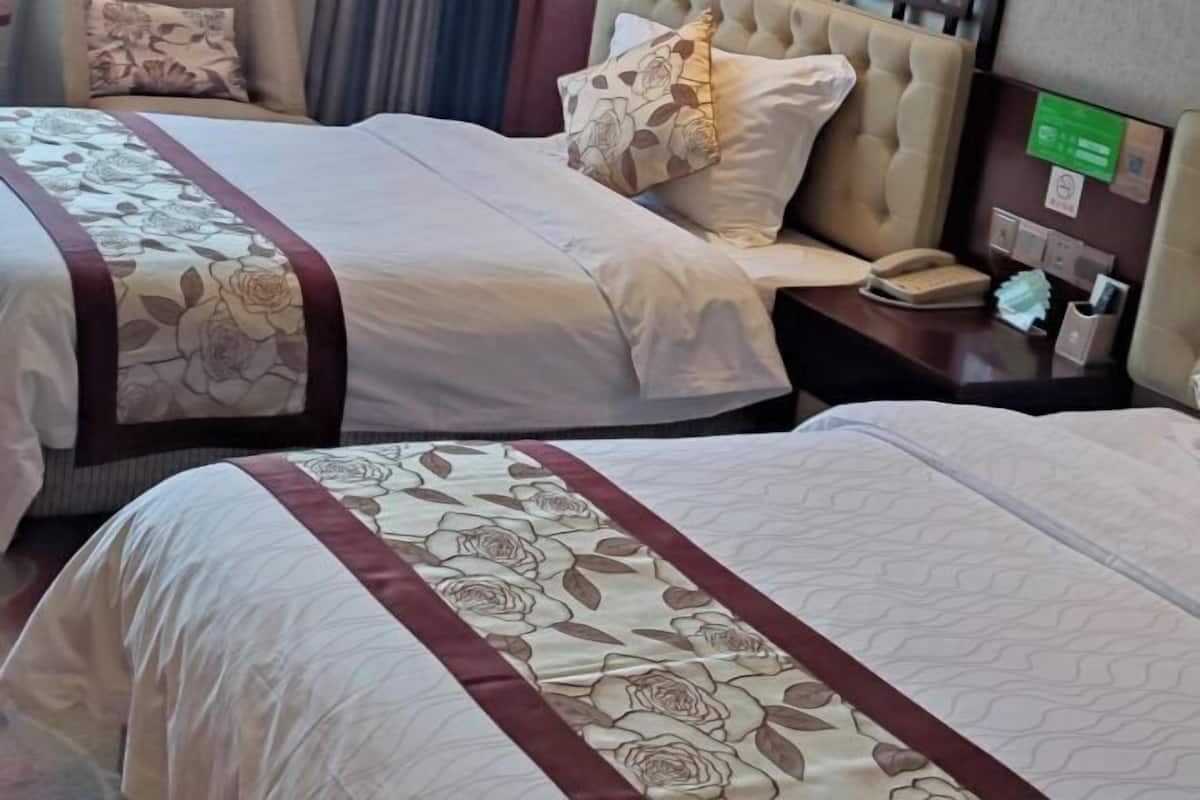 A hotel room with two beds, each with floral-patterned bedding and a red trim. There is a bedside table with a phone and a small lamp.