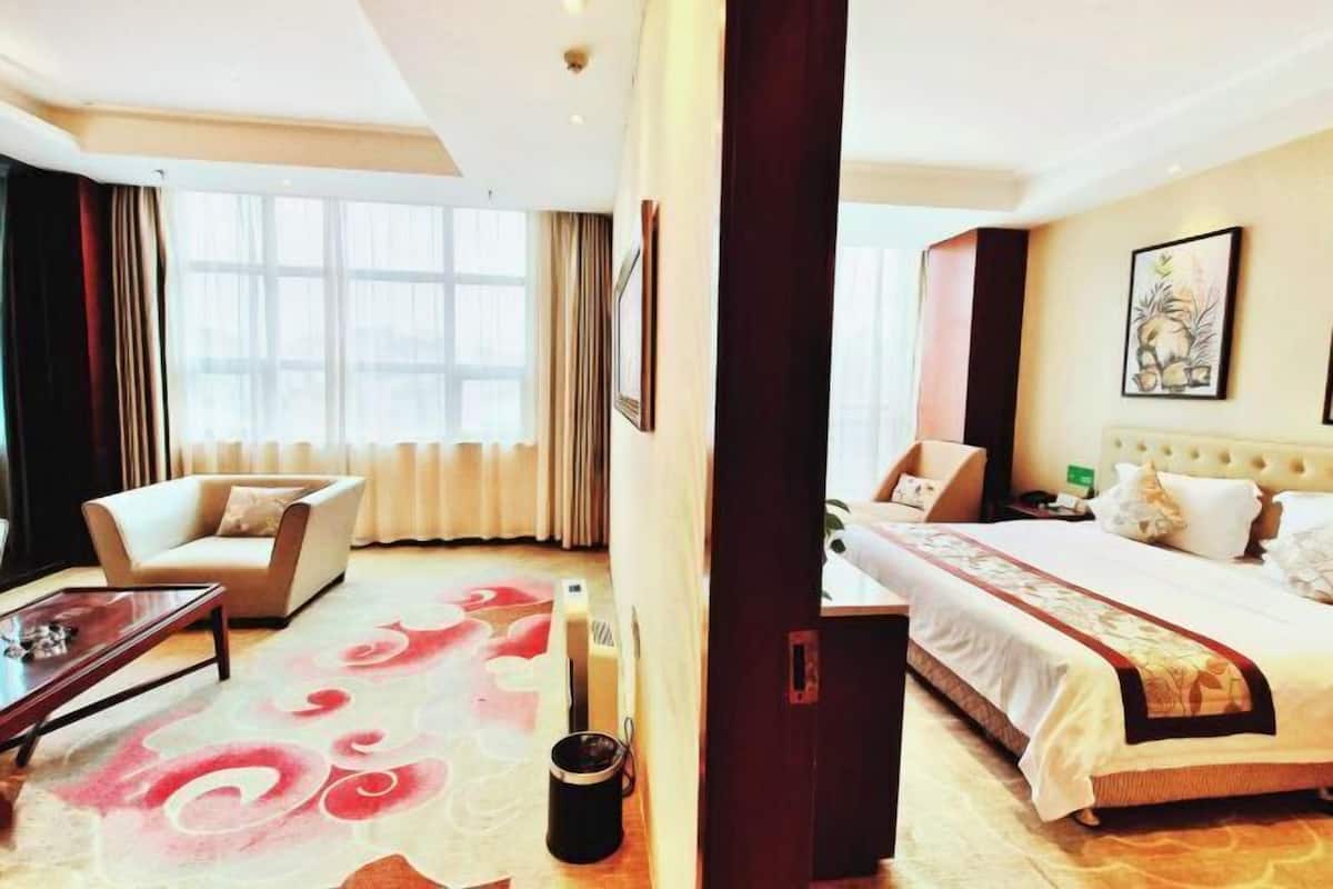 A hotel room with a bed, a sofa, a coffee table, and a large window.