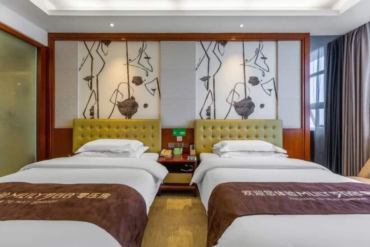 A hotel room with two beds, a wooden headboard, a wall art piece, a nightstand, and a window with curtains.