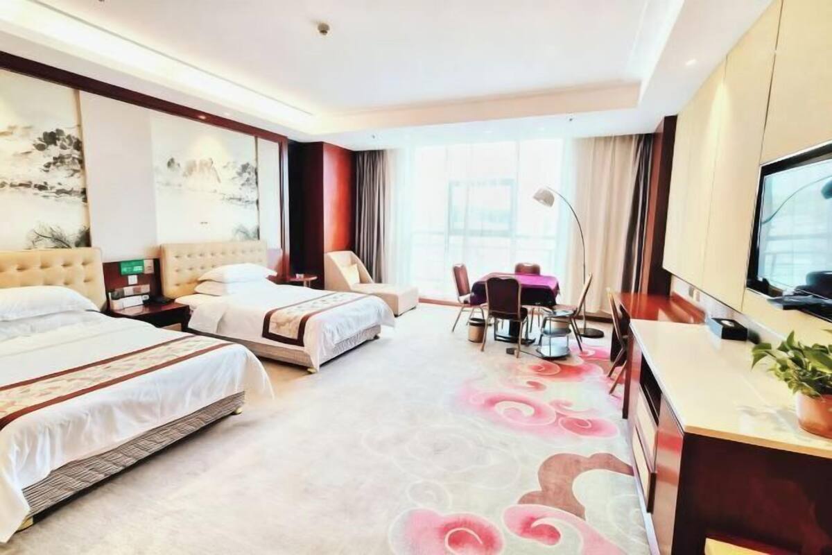A hotel room with two beds, a desk, a chair, a TV, and artwork on the walls.