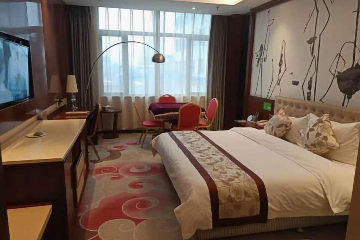 A hotel room with a bed, desk, chair, and a TV.