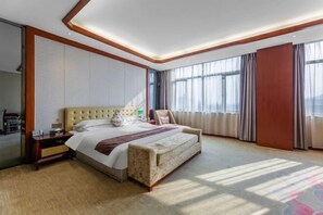 A hotel room with a large bed, a sofa, a nightstand, and a view of the city through large windows.