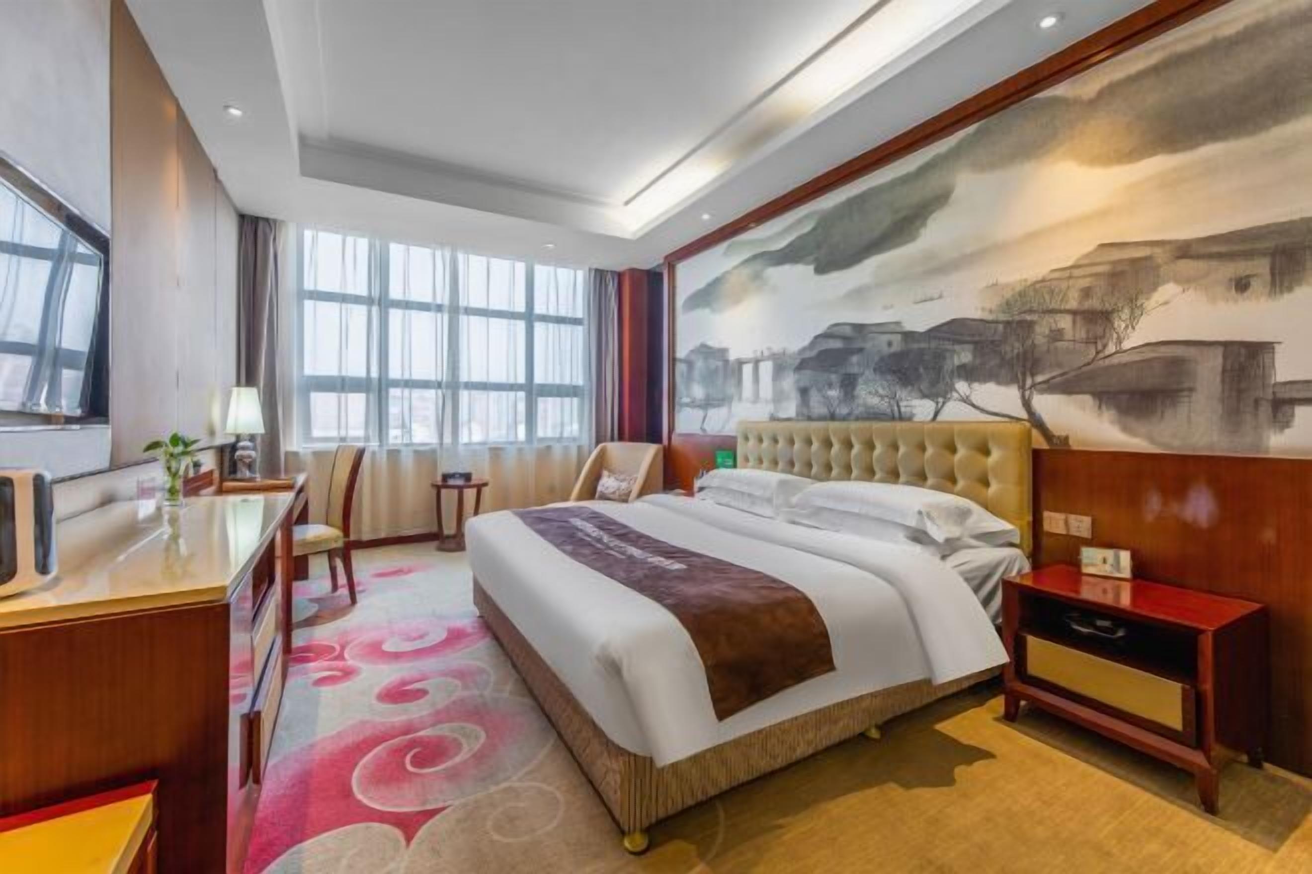 Habitación de hotel con una cama grande, un escritorio, una silla y un cuadro en la pared.