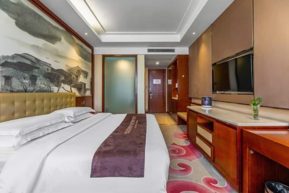 A hotel room with a large bed, a flat-screen TV, a desk, and a painting on the wall.