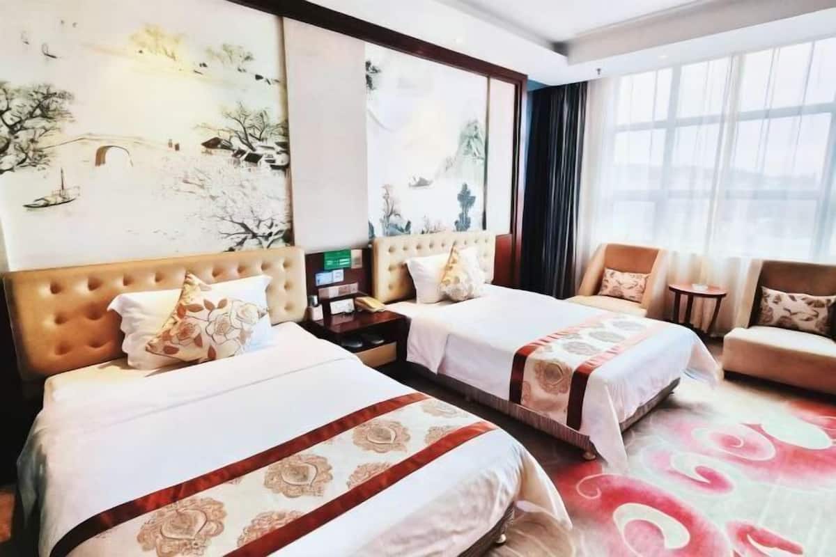 A hotel room with two beds, a sofa, a nightstand, and artwork on the walls.