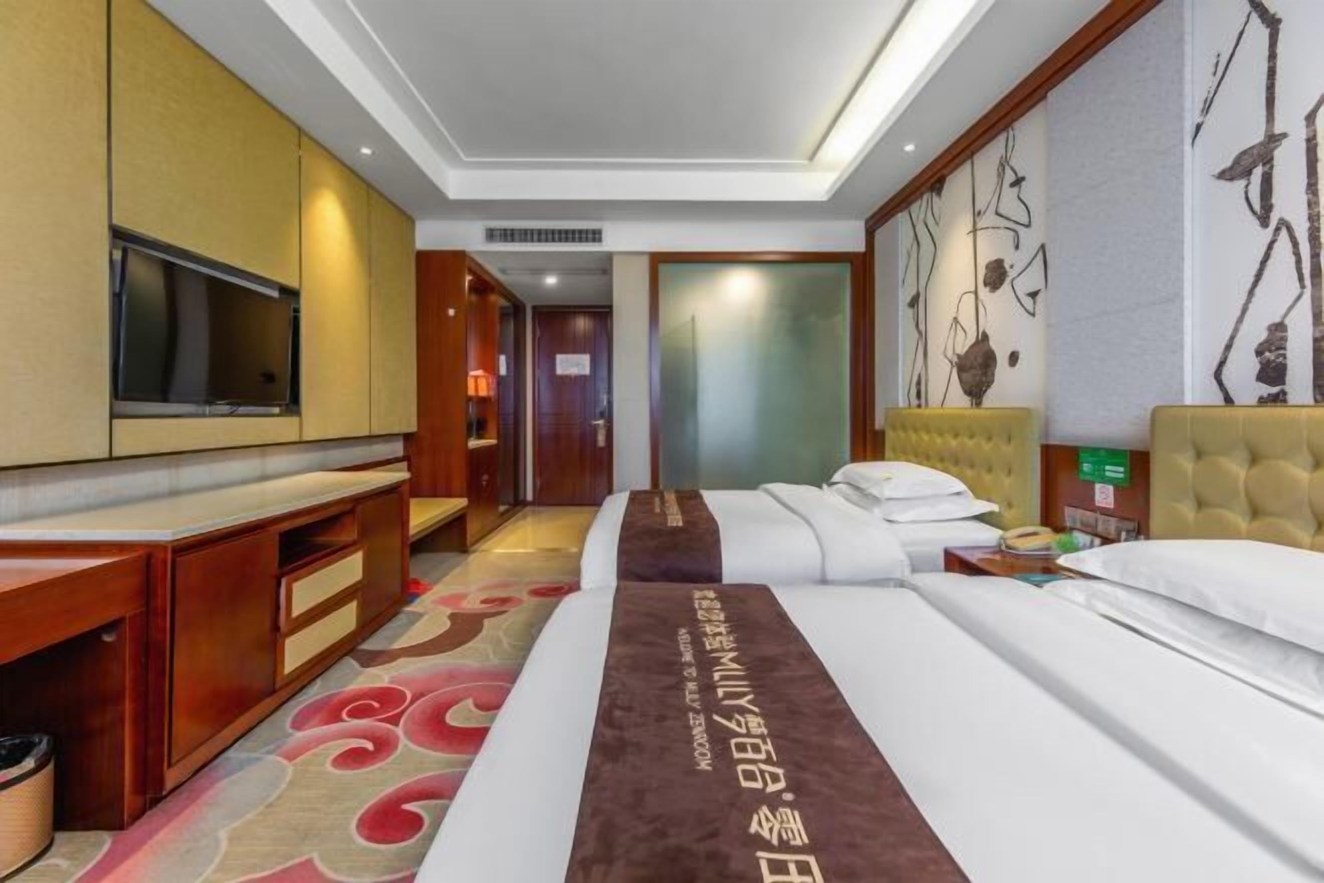 Ein Hotelzimmer mit Bett, Fernseher, Schreibtisch und einem Teppich mit Muster.