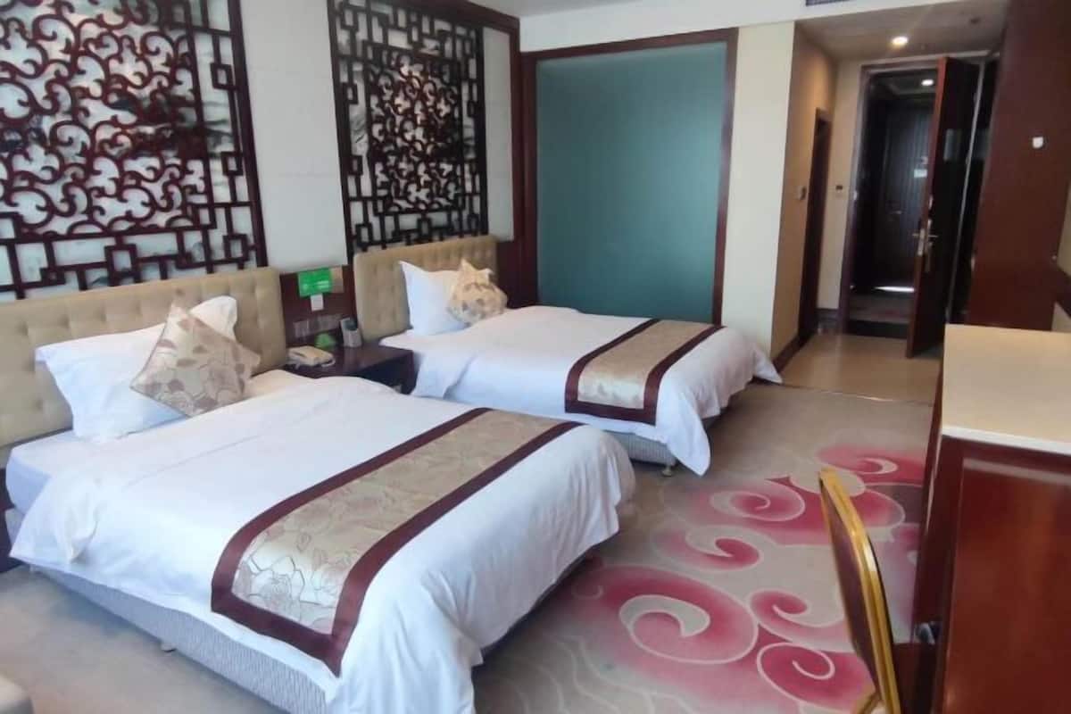 A hotel room with two beds, a decorative wall, a door, and a small table.
