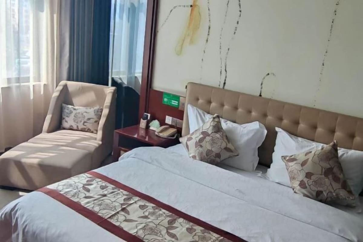 Una habitación de hotel con cama, una silla, una mesita de noche y una pared decorada con un cuadro.