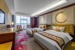 Habitación de hotel con dos camas, un escritorio, una silla, un ventanal grande y obras de arte en las paredes.