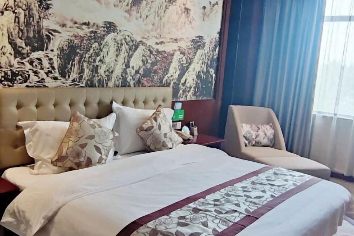 Una habitación de hotel con una cama grande, una silla, una mesita de noche y un cuadro en la pared.