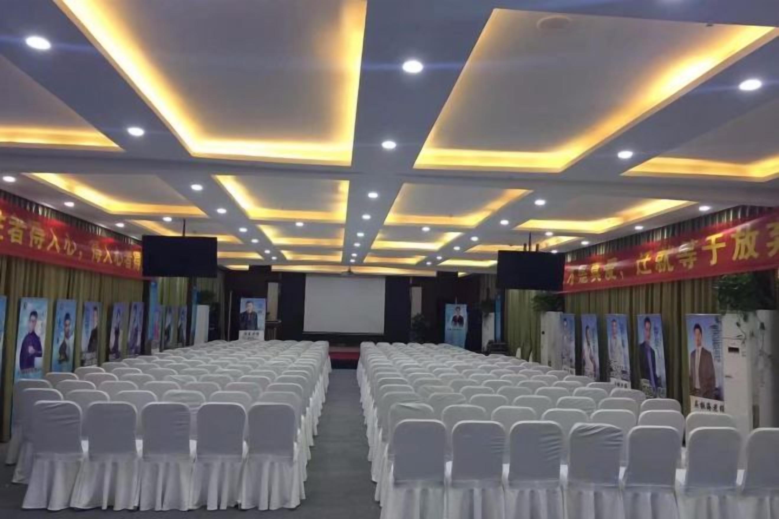 A conference room with rows of white chairs, a stage, and a screen.