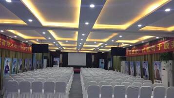 A conference room with rows of white chairs, a stage, and a screen.