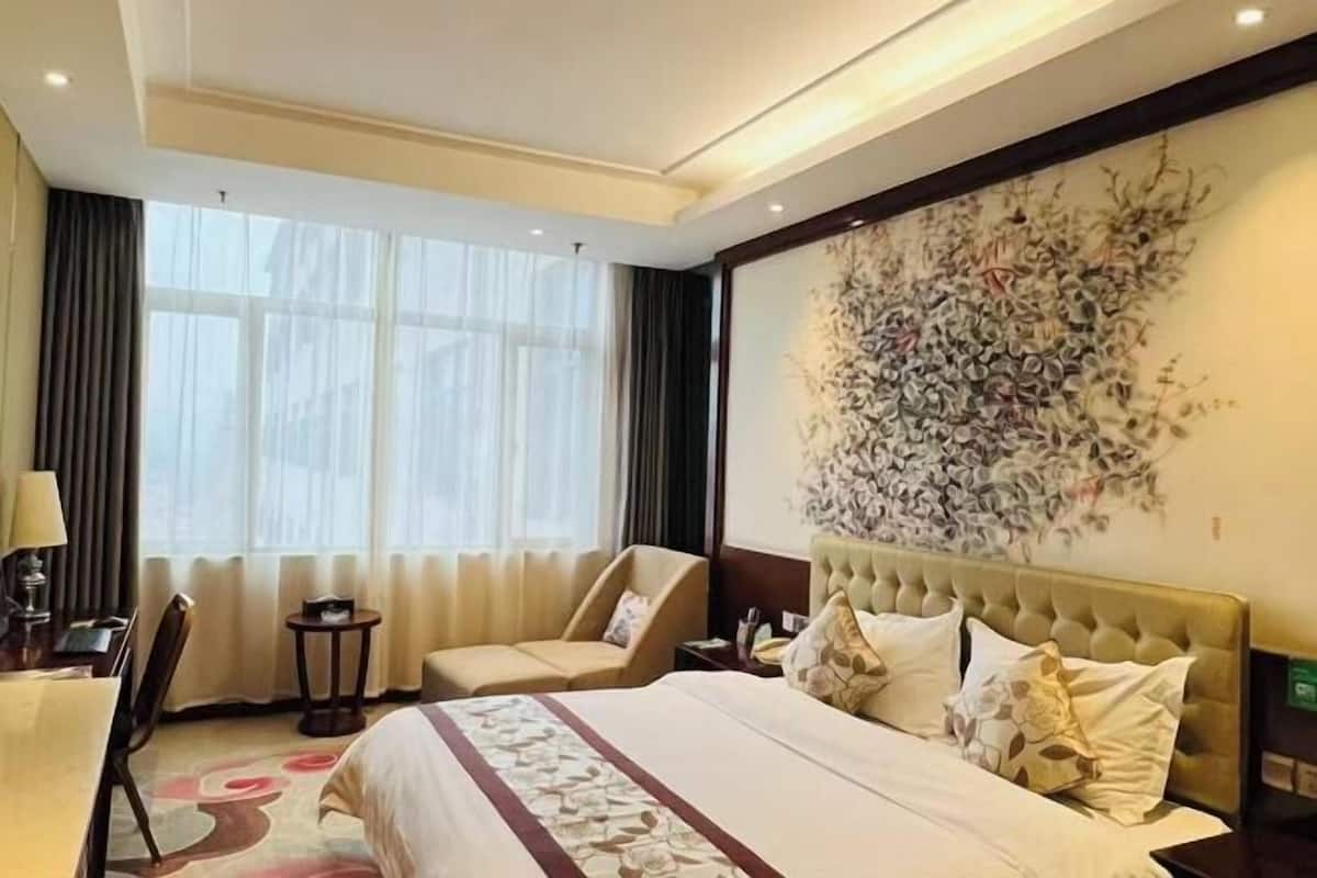 A hotel room with a large bed, a chair, a small table, and a decorative wall piece.