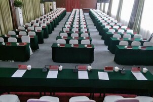 Un salón de conferencias con mesas y sillas dispuestas en filas, tarjetas de identificación y micrófonos.