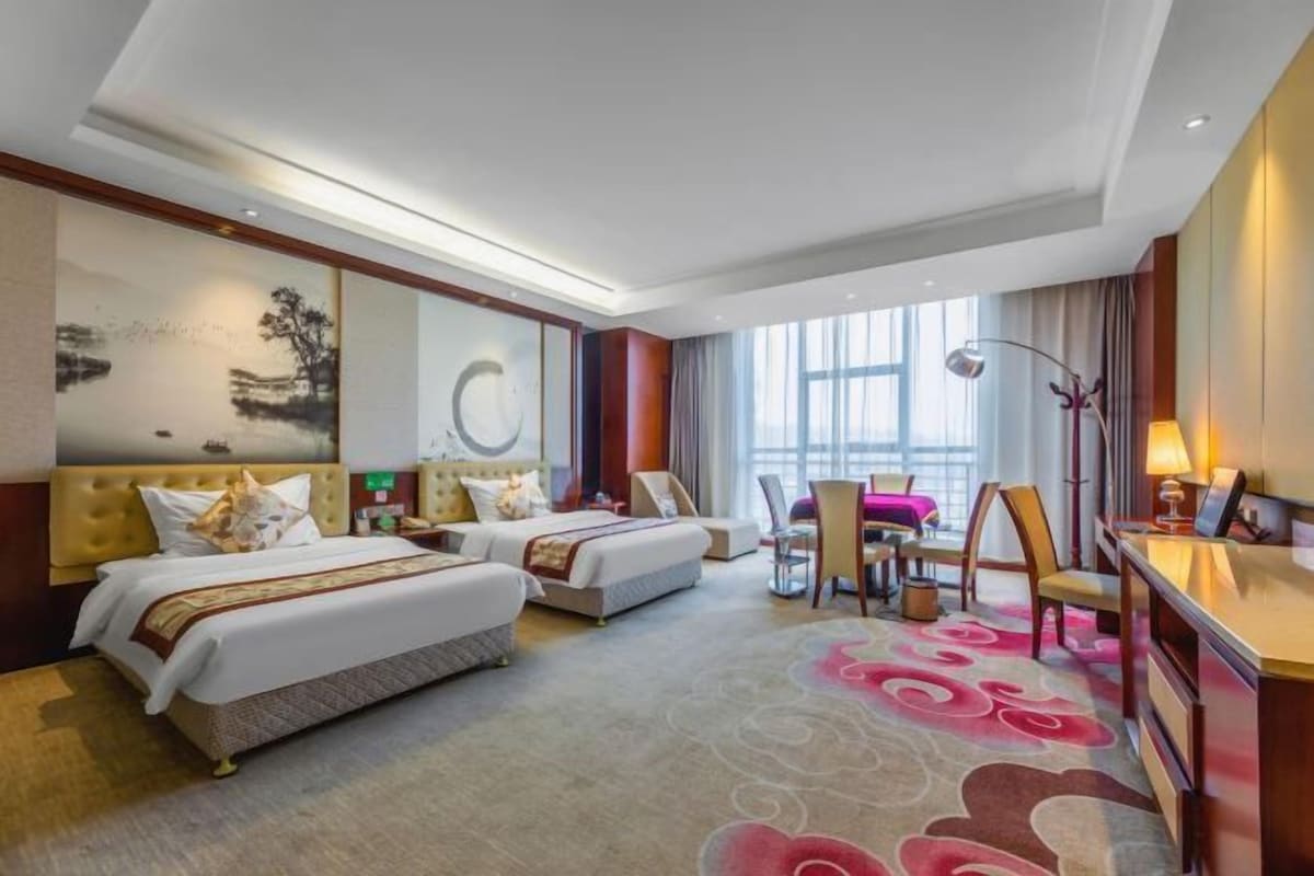 Habitación de hotel con dos camas, un escritorio, una silla, una mesa de comedor y un ventanal grande.
