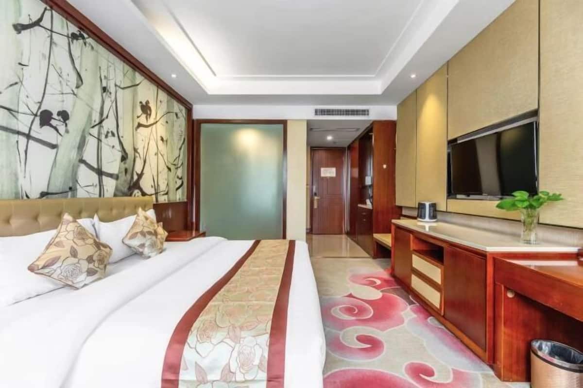 A hotel room with a bed, a TV, a desk, and a large window.