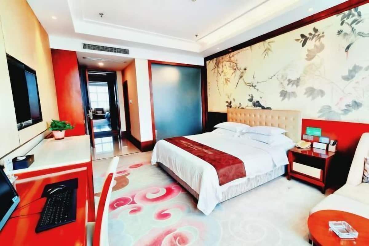 A hotel room with a bed, a desk with a computer, a nightstand, and a TV.