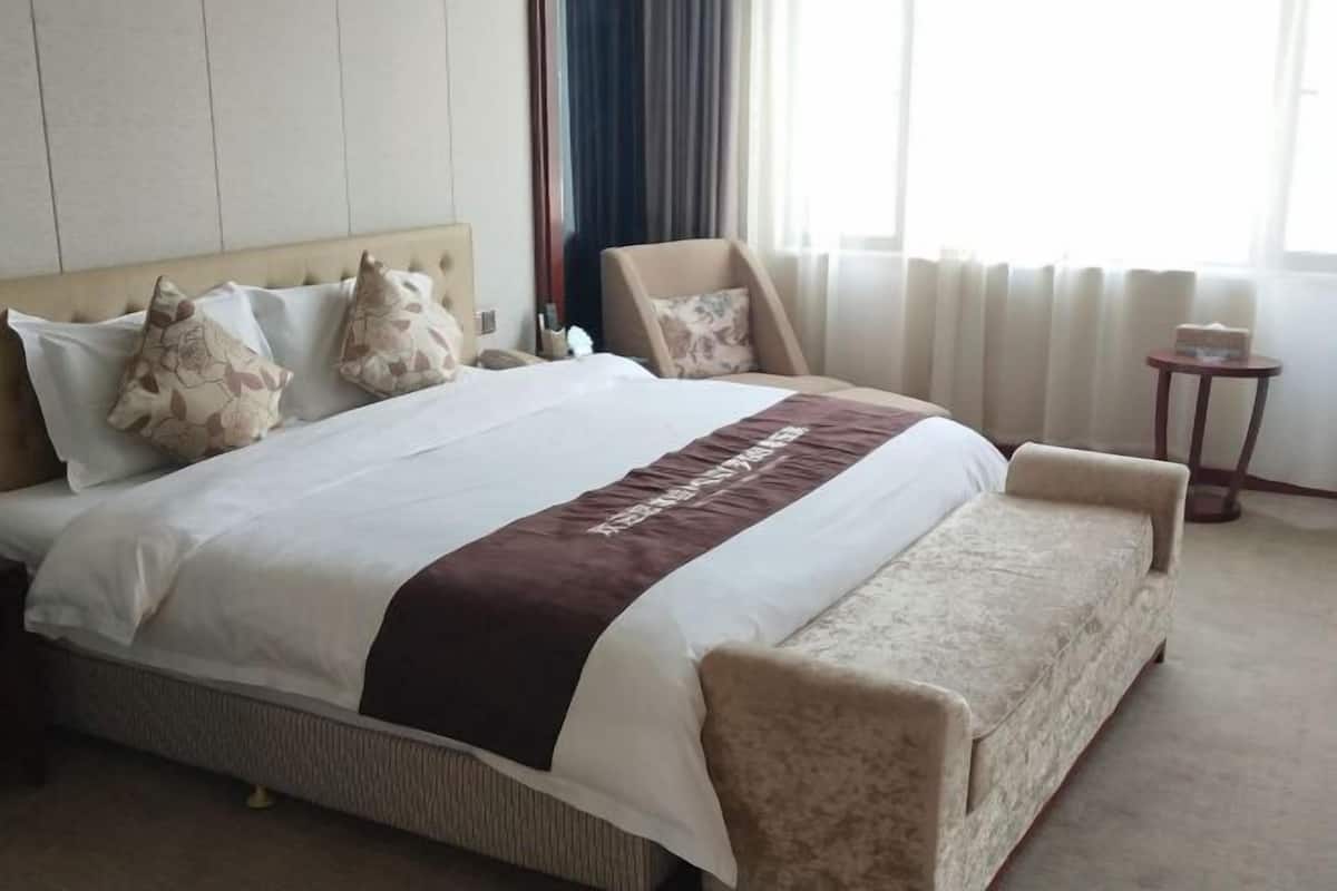 A hotel room with a bed, a chair, a small table, and a window with curtains.