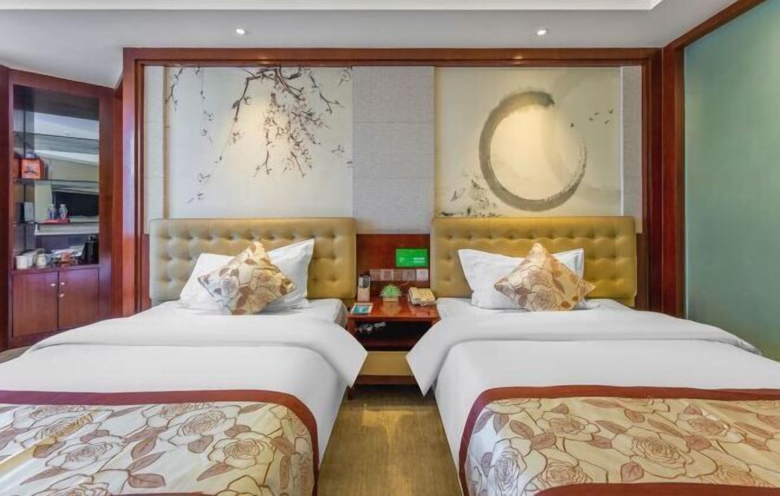 Quarto de hotel com duas camas, cabeceira de madeira, parede com desenho circular e mesinha de cabeceira com abajur.