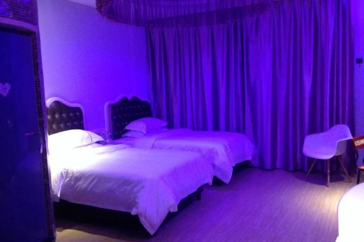 A hotel room with two beds, a chair, and a curtain.