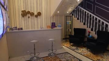 Un área de recepción con mostrador, dos taburetes, una escalera y una sala de estar con sillas.