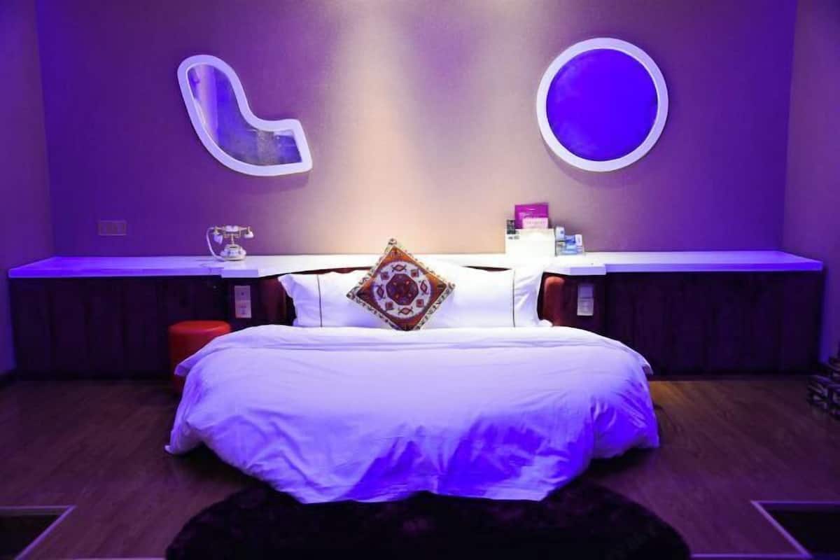 A modern bedroom with a large bed, a bedside table, and a wall-mounted mirror.