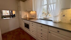 A kitchen with white cabinets, a stove, a sink, and a window with sheer curtains.