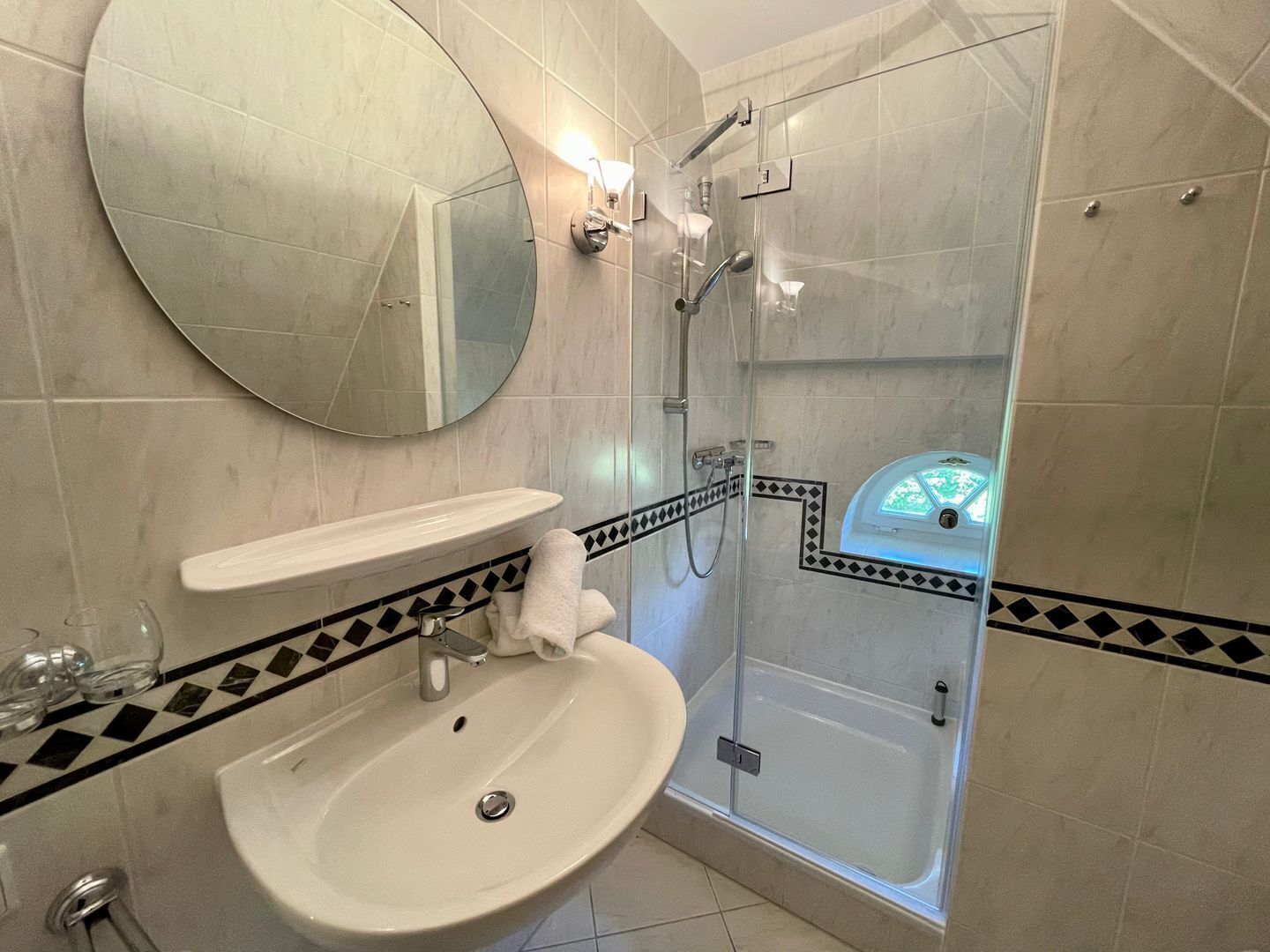 A bathroom with a round mirror, a sink, a shower enclosure, and a bathtub.