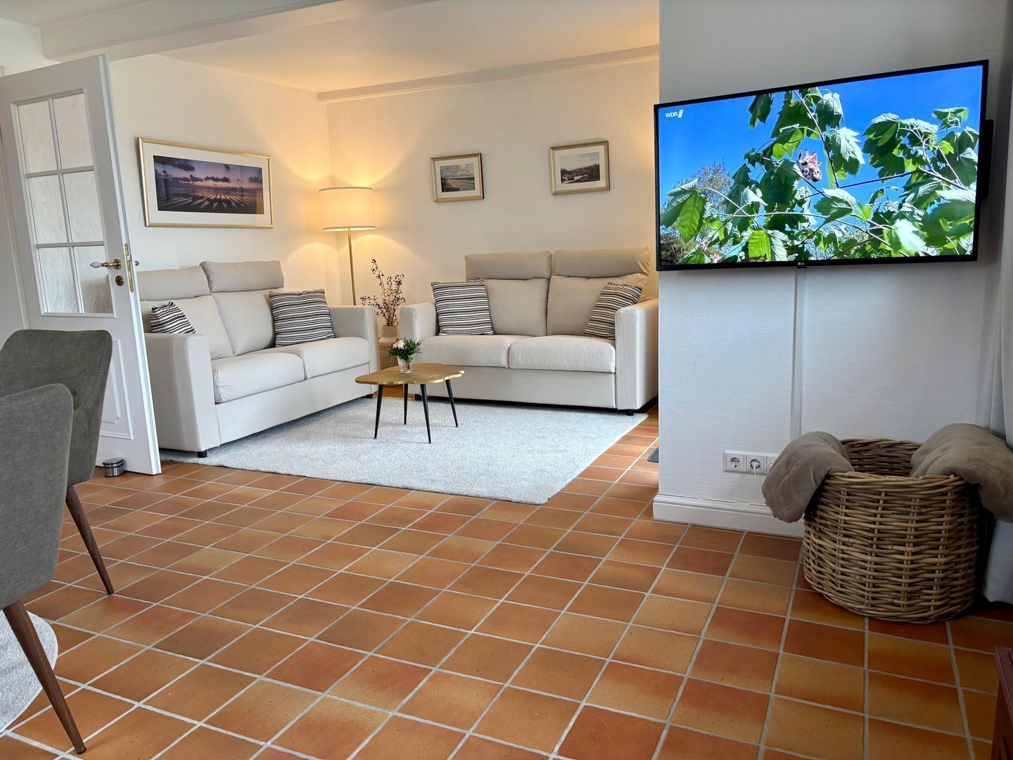 Ein Wohnzimmer mit zwei weißen Sofas, einem Couchtisch, einem Fernseher und einem Korbwannen-Korb.