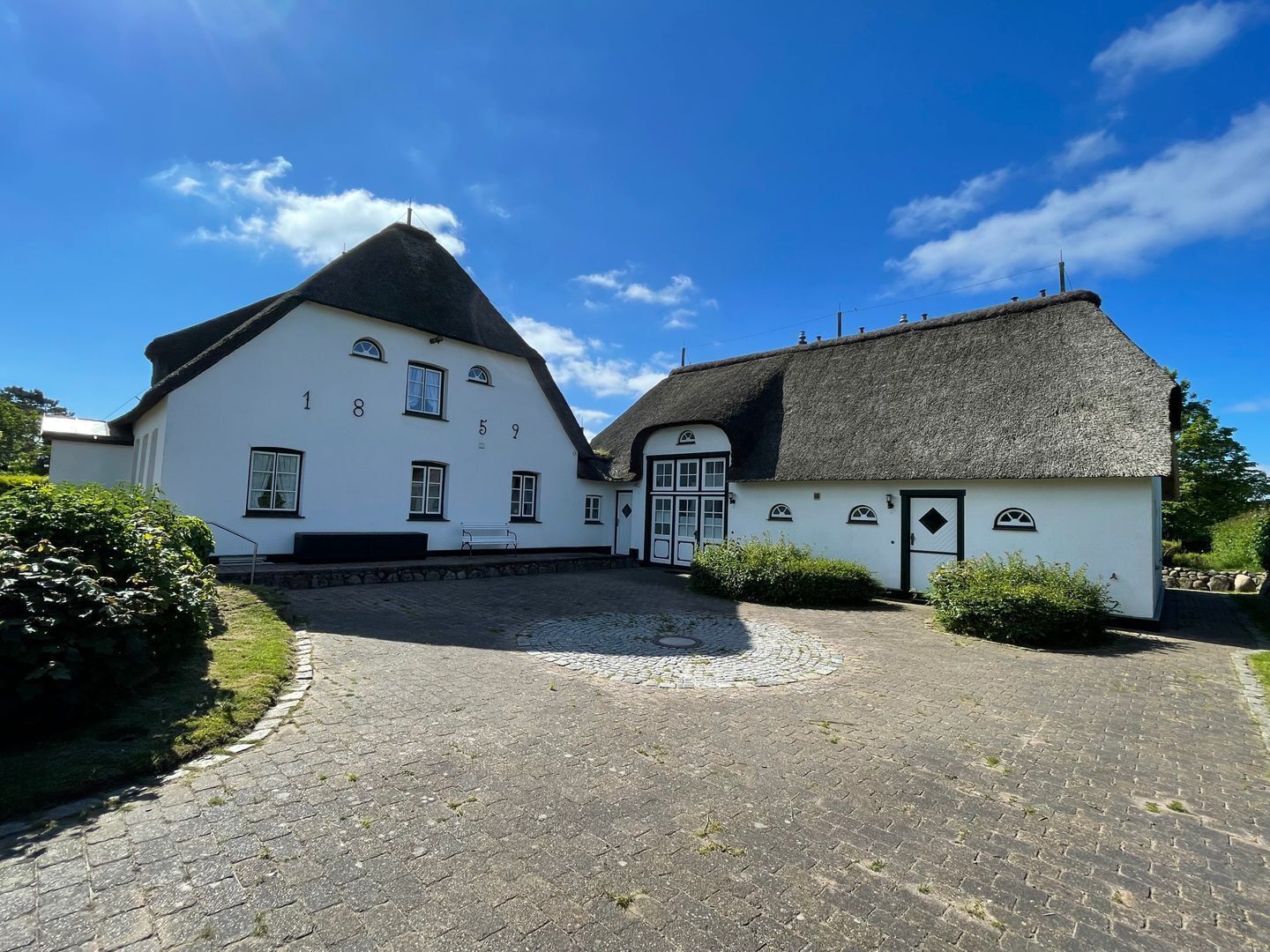 En traditionell byggnad med ett halmtak, vita väggar och en uppfart belagd med kullersten.
